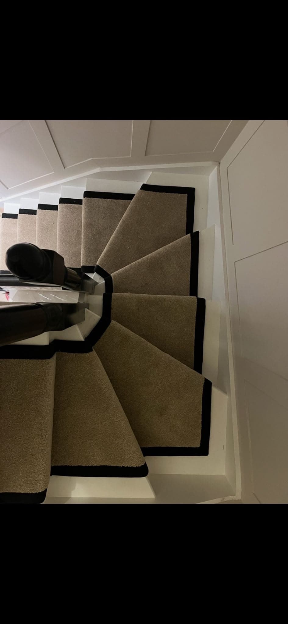 Tan carpet with black border trim fitted on a curved staircase
