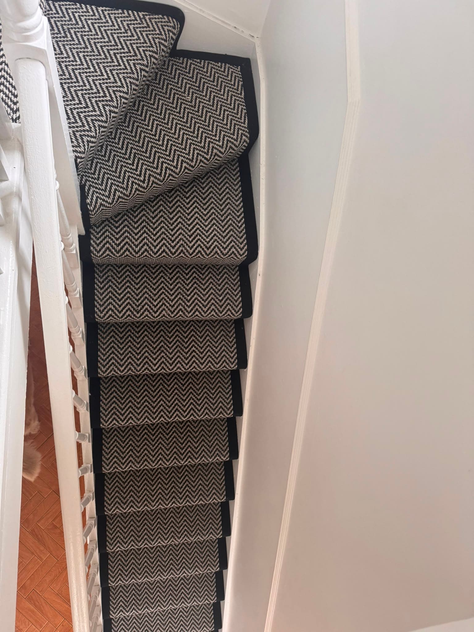 Tan herringbone-weave carpet runner with brown border trim fitted on a staircase