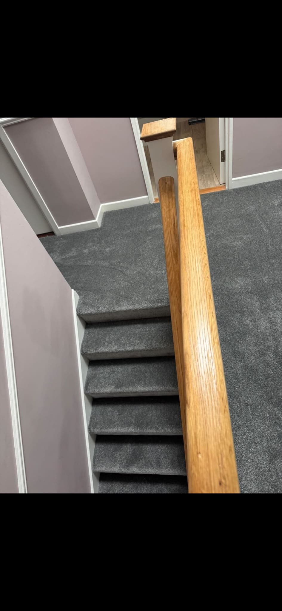 Dark grey carpet fitted on a staircase with a varnished oak handrail and white balusters