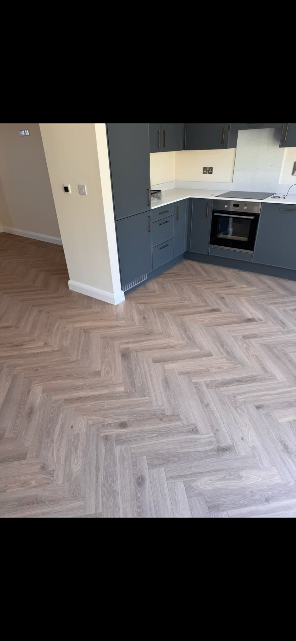 Herringbone-pattern laminate flooring fitted in a kitchen with navy cabinetry
