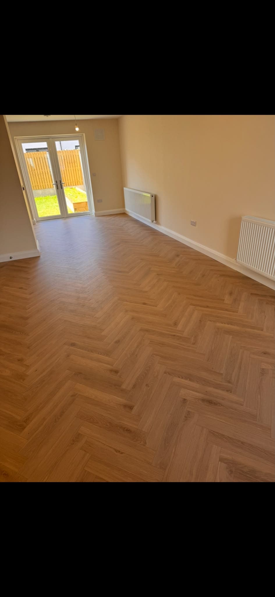 Herringbone-pattern laminate flooring fitted in a bright room with patio doors
